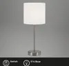 A table lamp with a white shade and a silver base and stem, set against a plain gray background. Icons and text indicating 'Switch' and 'E14 Base' are visible at the bottom. Produktbild-Vorschau