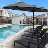 A patio umbrella shades a swimming pool and lounge chairs at a residential complex. Produktbild-Vorschau