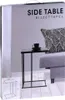 A black side table with a cup of coffee on it, placed next to a gray sofa with a patterned cushion. Podgląd zdjęcia produktu