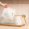A hand holding a bag of collagen powder next to a container and a scoop. Produktbild-Vorschau