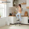 A woman is using a step stool in a kitchen to reach a cabinet. Produktbild-Vorschau