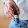 A hand holding a small roll-on bottle of essential oil, placing it into a jeans pocket. Náhľad obrázku produktu