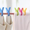 Several colorful plastic clothespins are holding a white towel and two beige slippers on a wooden rod. Produktbild-Vorschau