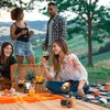 A group of friends enjoying a picnic in a scenic outdoor setting, with wine and food laid out on a blanket. Produktbild-Vorschau