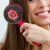 Rote Haartrocknerbürste mit schwarzen Borsten und roten LED-Leuchten, gehalten von einer Frau, die ihr langes braunes Haar bürstet Produktbild-Vorschau