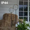 Two spherical LED light decorations are placed in front of hay bales and flowers, with a house visible through a window in the background. Produktbild-Vorschau
