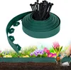 A roll of green garden edging and black stakes are shown in the foreground, with a blurred background of flowers and soil. Náhled obrázku produktu