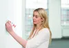 A woman is applying a product from a tube to a white wall. Produktbild-Vorschau