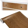 A collage showing a roll of wood-grain contact paper and a close-up of wood-grain drawer fronts on a white piece of furniture. Produktbild-Vorschau