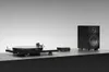A turntable and a speaker are displayed on a black surface against a light gray background. Produktbild-Vorschau