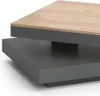 A close-up, angled view of a modern coffee table with a two-tiered design. The top surface is a light wood grain, and the base is a dark grey, matte finish. Voir les images du produit