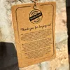 A close-up of a product tag hanging from a string against a stone wall. Podgląd zdjęcia produktu