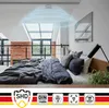 A bedroom with a bed covered in dark gray bedding, a skylight window, and a smoke detector on the ceiling emitting blue rings to indicate its function. Produktbild-Vorschau