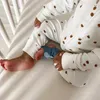 Close-up of a baby's legs wearing a white pajama with brown dots and a blue sock on one foot. Produktbild-Vorschau