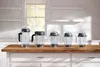 Five Vitamix blender containers of different sizes are lined up on a wooden countertop in a bright kitchen. Anteprima dell’immagine prodotto