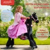 A young girl in a pink dress rides a black toy horse with pink accents in an outdoor setting. Anteprima dell’immagine prodotto
