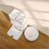 A white robot vacuum cleaner and its charging/emptying station are shown on a wooden floor next to a wall. Náhled obrázku produktu