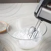 A hand mixer is whipping cream in a glass bowl, with a wooden scoop of flour in the background. Produktbild-Vorschau