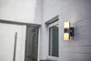 An outdoor wall light is mounted on a white brick wall next to a door and window. Anteprima dell’immagine prodotto