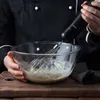 A person in a black chef's jacket is using a hand blender to mix ingredients in a glass bowl. Produktbild-Vorschau