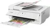 A white Canon PIXMA TS9551Ca printer is shown from a slightly elevated front-left angle, with a printed document emerging from the output tray and papers loaded in the input tray. Podgląd zdjęcia produktu