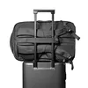 A black backpack is attached to the handle of a rolling suitcase. Produktbild-Vorschau