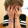 A child is covering their face with their hands, wearing multiple colorful bracelets. Podgląd zdjęcia produktu