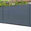A dark gray metal fence with horizontal slats, supported by vertical posts. Green foliage and a hint of a red roof are visible behind the fence. Produktbild-Vorschau