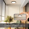 A hand holding a smartphone showing a reflection of a ceiling light, with the actual ceiling light visible above. The scene is set in a modern room with blinds and plants. Produktbild-Vorschau
