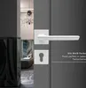 A white door handle and keyhole plate are shown on a dark gray door, with a glimpse into a room with a chandelier and marble-like columns in the background. Produktbild-Vorschau