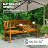 A wooden garden bench with a small table between the seats, set outdoors with greenery and an umbrella. Anteprima dell’immagine prodotto