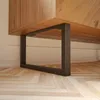 A close-up view of a black metal furniture leg attached to a wooden cabinet, resting on a wooden floor. Náhľad obrázku produktu