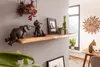 A wooden shelf with decorative elephant figurines and plants, set against a gray wall in a room with a window and dining table. Náhled obrázku produktu