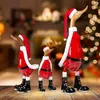 Three wooden ducks dressed as Santa Claus are displayed on a wooden surface in front of a blurred background with a fireplace and Christmas lights. Produktbild-Vorschau