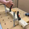 A person's hand is shown adjusting a clamp on a piece of wood, which is part of a larger woodworking project. A drill and other tools are visible in the background. Náhľad obrázku produktu