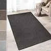 A dark gray rug is shown on a light wooden floor, with a sofa and curtains in the background. Several swatches of different colored rugs are displayed on the left side of the image. Produktbild-Vorschau