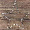 A silver wire star ornament hangs against a wooden background. Produktbild-Vorschau