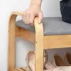 A hand is shown resting on the top of a wooden shoe rack with a gray cushion. Produktbild-Vorschau