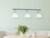 A three-light pendant lamp with white glass shades hangs above a table with a plant and a mug. Produktbild-Vorschau