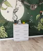 A white dresser with drawers is placed in front of a jungle-themed mural. The mural features various animals like a sloth, lemur, and toucan, along with lush foliage and a large moon. Náhled obrázku produktu