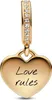 A gold heart-shaped charm with the words "Love rules" inscribed on it, hanging from a gold bail adorned with small clear stones. Voir les images du produit