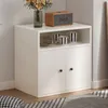 A white cabinet with two doors and an open shelf on top, decorated with a vase of flowers and a speaker. Produktbild-Vorschau