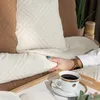 A person's hand rests on a beige quilted blanket on a bed, with a cup of coffee on a tray in the foreground. Produktbild-Vorschau