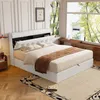 A bedroom with a white upholstered bed, a large window with trees outside, and wooden furniture. Produktbild-Vorschau