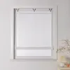 A white roller blind with a subtle pattern is installed in a window frame. A small lamp and a decorative branch are visible on a nightstand to the right. Produktbild-Vorschau