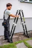 A man is holding a multi-purpose ladder next to a building. Náhľad obrázku produktu