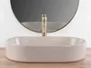A beige matte washbasin with a gold faucet in front of a round mirror. Produktbild-Vorschau