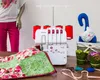 A sewing machine with spools of thread, a quilt, and decorative items on a table. Náhled obrázku produktu