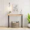 A console table with a wooden top and metal legs, decorated with a plant, books, and candlesticks, placed against a white wall. Produktbild-Vorschau