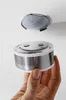 A hand holding a smoke detector base with a mounting bracket attached to a white ceiling above. Produktbild-Vorschau